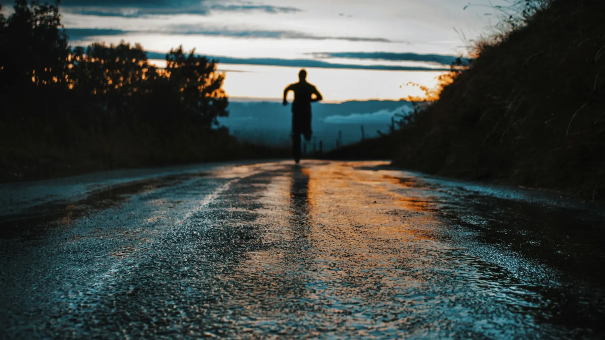 Silueta de un corredor en una carretera mojada al atardecer
